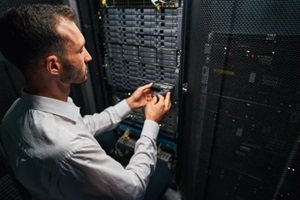handsome caucasian system administrator controlling operational server rack in room indoors