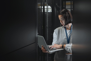 Woman with laptop, datacenter and information technology, engineer and server room with software update. Tech industry, cybersecurity and network with Asian female setting up firewall and database.