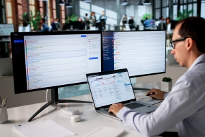 IT support professional managing multiple monitors displaying ticketing and quality management dashboards in a modern office environment