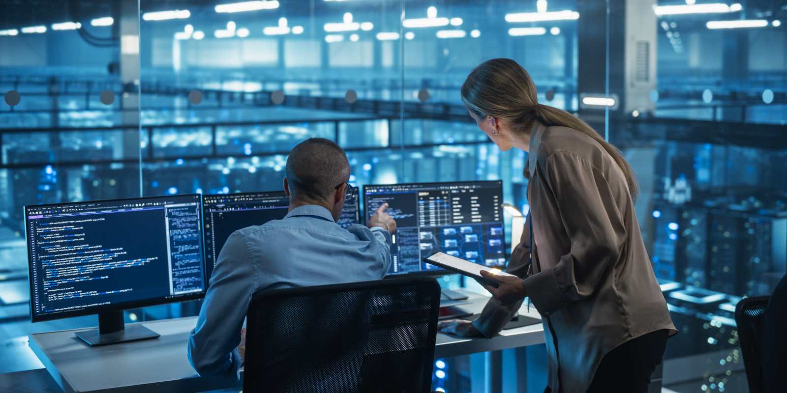 IT consultant and client reviewing network data on monitors in a managed IT services office