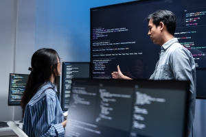 IT professionals discussing code on multiple monitors during a technical review