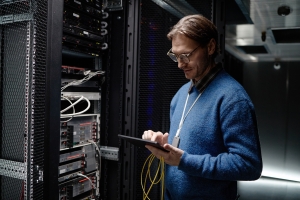 IT technician using a tablet to manage network servers in a data center rack room