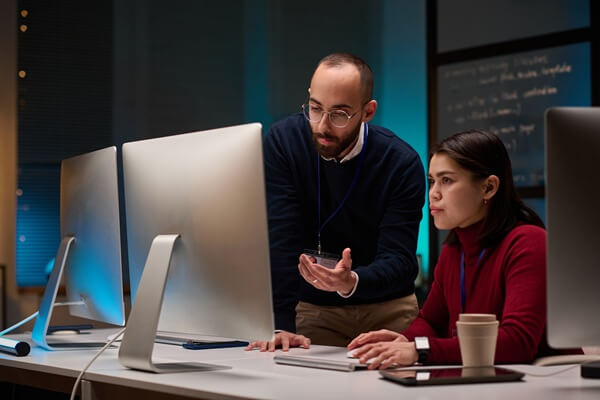 minimal portrait of two people using computers while working in cybersecurity department with blue lights