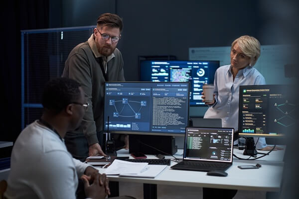 multiethnic business team reviewing cybersecurity data on monitors, discussing network analysis in office