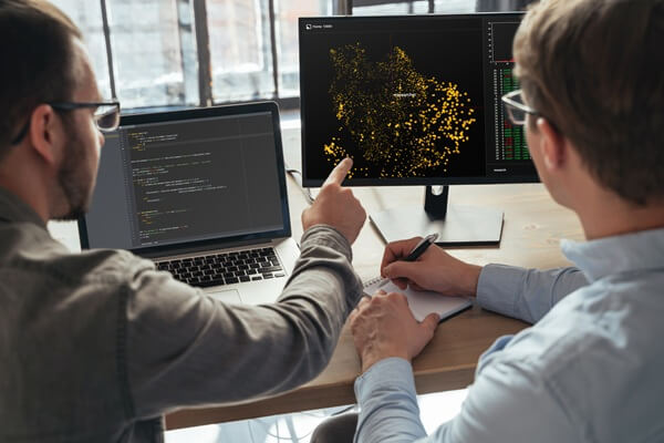 two men data science specialists working at office together, analyzing big data on screen