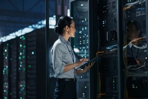 asian female network technician standing with digital tablet computer in front of open server rack cabinet