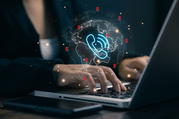 professional types on a laptop with a global phone network hologram, representing VoIP communication